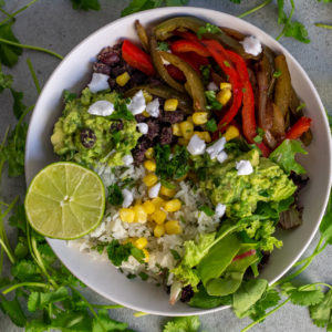 Veggie fajita burrito bowl with lime, cilantro, rice, corn, guacamole, black means