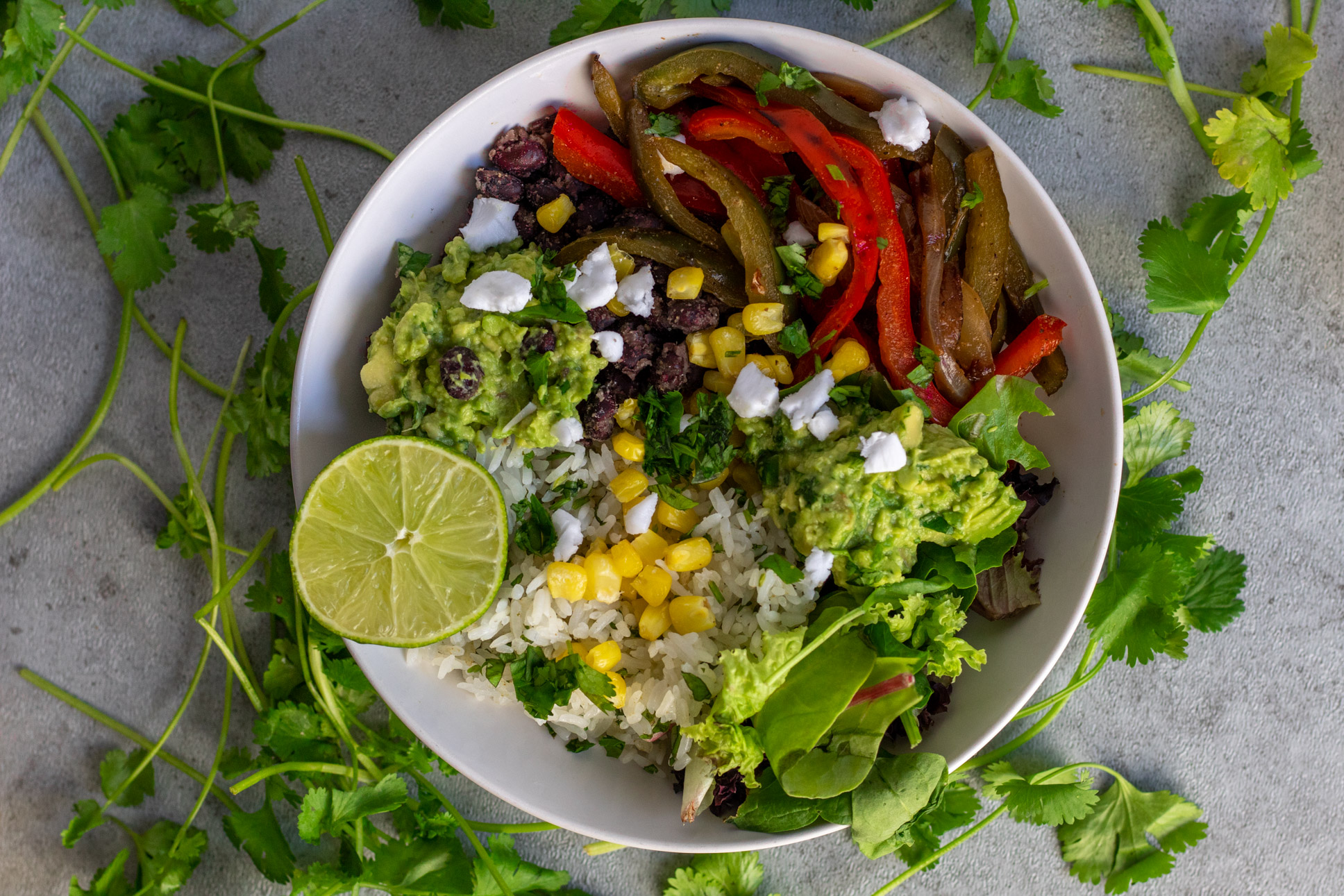 Veggie fajita burrito bowl with lime, cilantro, rice, corn, guacamole, black means